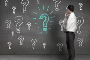 Businessman looking at drawings of question marks drawn on a wall betonozas-gyakori-kerdesek